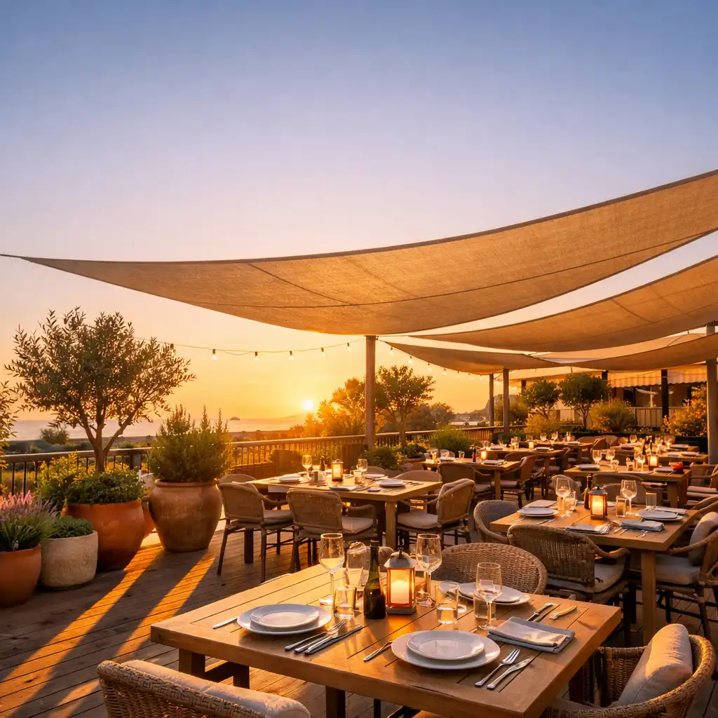 Terrasse du restaurant au coucher du soleil avec tables dressées et voiles d'ombrage